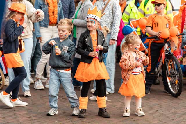 Kinderen in oranje kleding dansen en vieren samen het feest op straat.