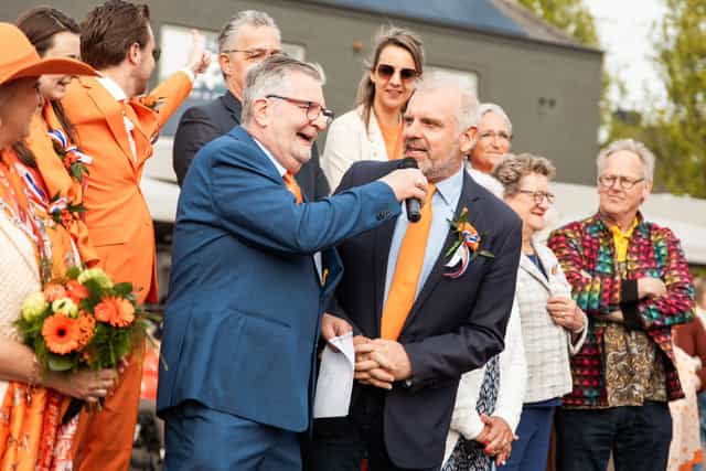 Interview op het dorpsplein tijdens een feestelijke bijeenkomst met oranje accenten.