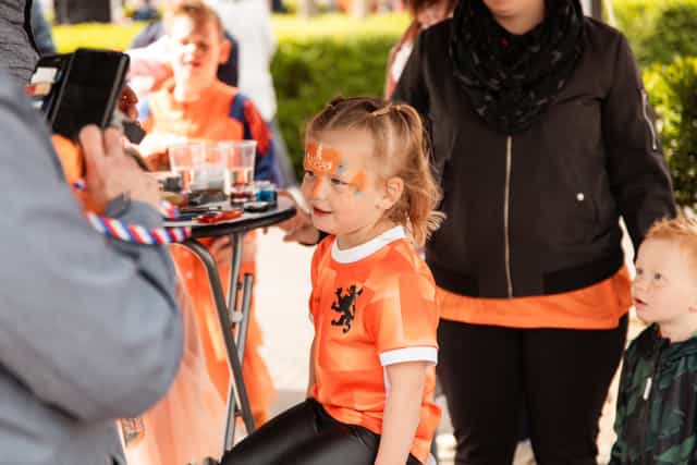 Meisje met oranje schmink kijkt naar een dienblad met schmink en feestspullen.